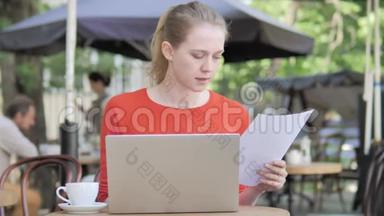 年轻女子阅读<strong>合约</strong>及使用电脑坐在咖啡厅露台